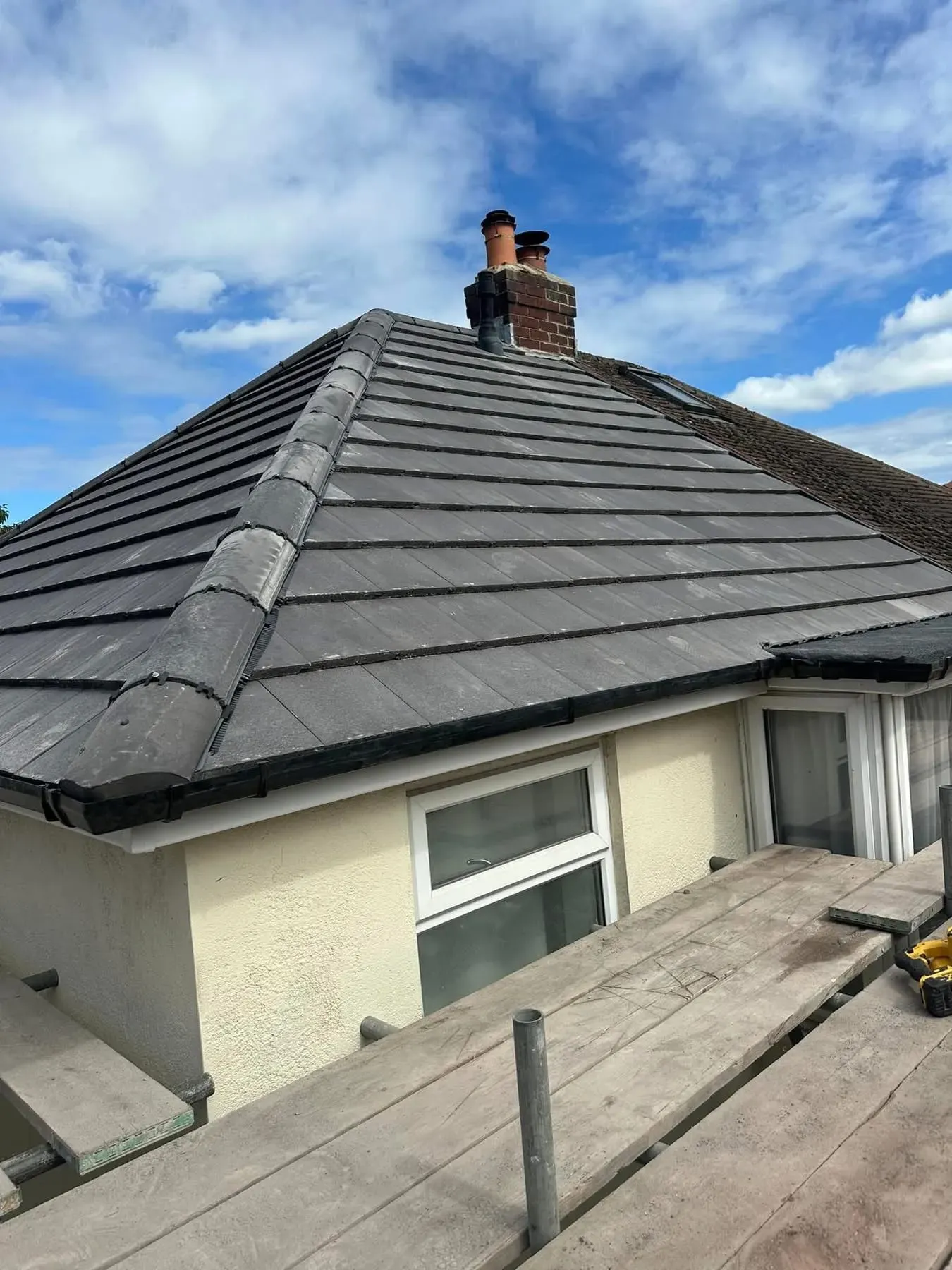 Expertly installed grey tile roofing on a house in Otley, Leeds, showing ridge tiles and chimney repairs with scaffolding.